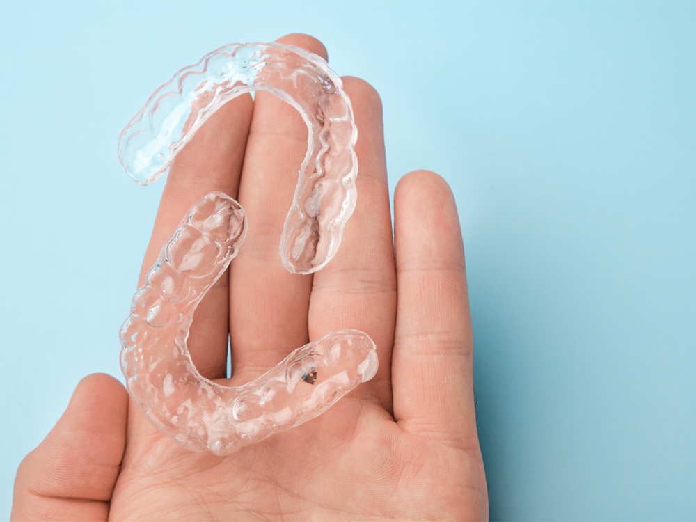 a hand holding clear retainers against a blue background