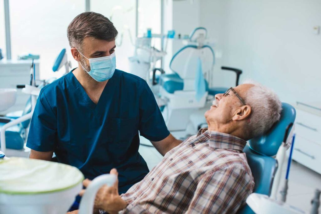 senior male sitting in a dental chair looking at a male dentist