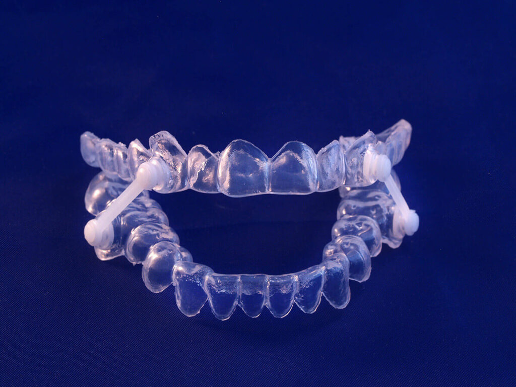 Close-up image of a transparent sleep apnea mask placed on a light blue background, highlighting the mask's detailed structure with tubing and adjustment straps, emphasizing medical respiratory assistance.